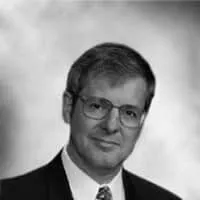 Professional headshot of a man in a suit and glasses, with a neutral background, suitable for corporate or business use.