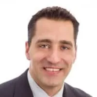 Professional headshot of a smiling man in a suit, showcasing a confident and approachable demeanor against a plain white background.