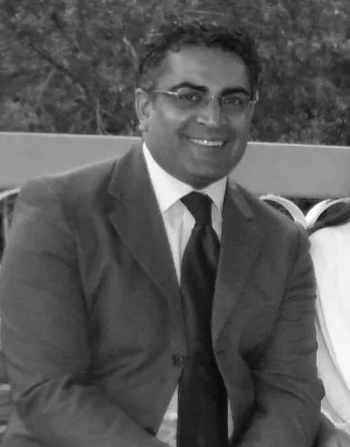 Smiling man in a suit sitting outdoors, showcasing a professional appearance and friendly demeanor.