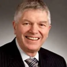 Professional headshot of a smiling man in a suit, showcasing a friendly demeanor and short gray hair.