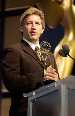 Man in a suit holding an Emmy Award while speaking at a podium during an awards ceremony.