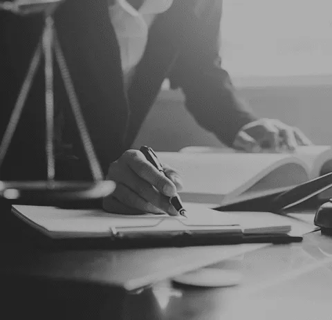 A lawyer writing notes in a legal office, with a scale of justice in the background and open law books on the desk, symbolizing legal research and case preparation.