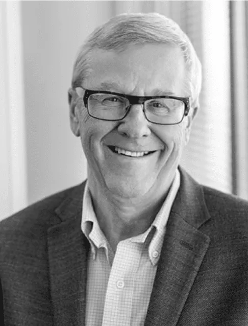 Smiling middle-aged man in glasses wearing a blazer, seated indoors with natural light, conveying a professional and approachable demeanor.