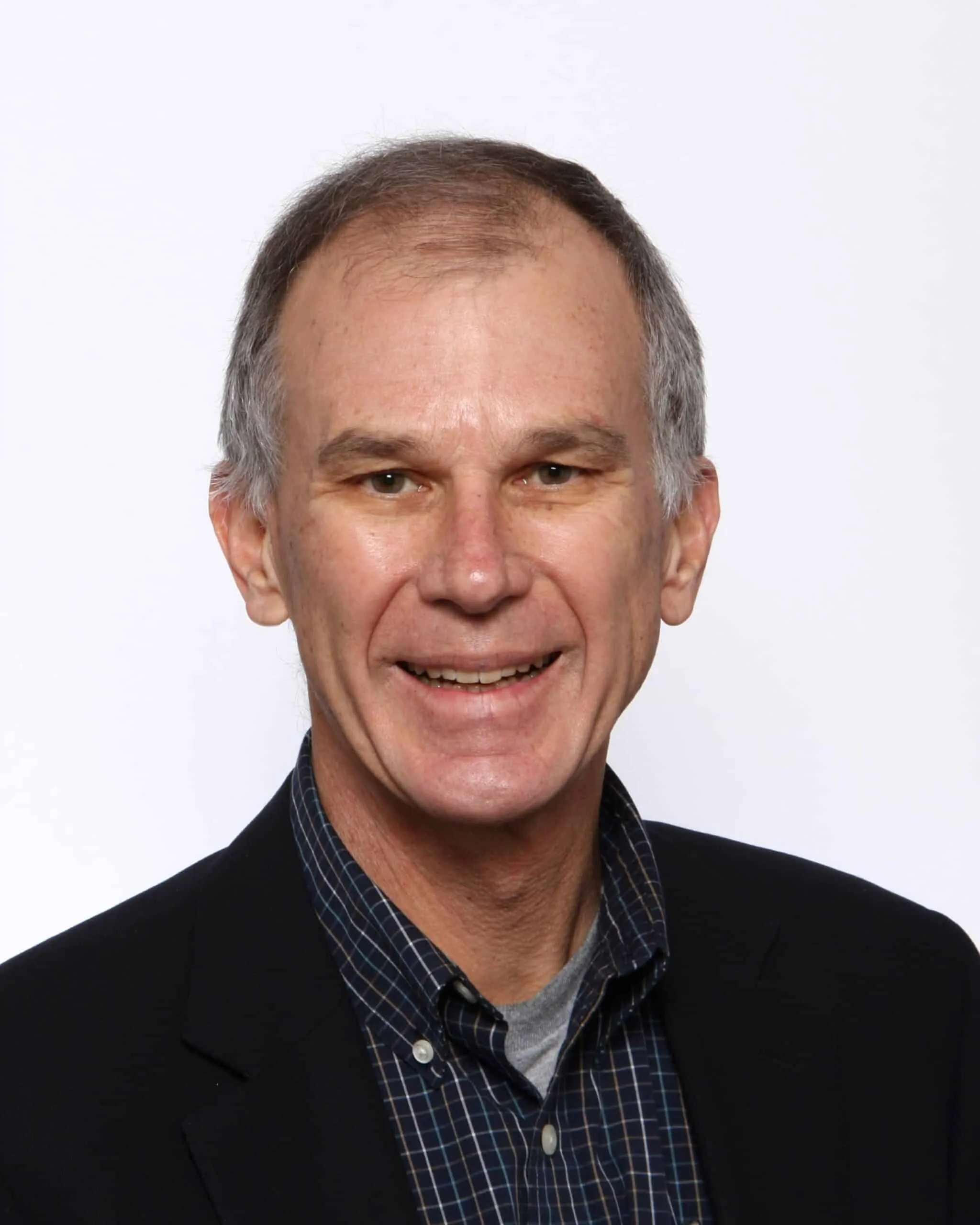 Smiling middle-aged man with short gray hair, wearing a black blazer over a checkered shirt, against a plain white background.