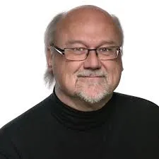 Professional headshot of a middle-aged man with glasses and a slight smile, wearing a black turtleneck sweater. The background is plain white, emphasizing his features and expression.