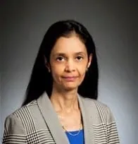 Professional headshot of a woman with long black hair, wearing a gray blazer over a blue top, set against a neutral background.