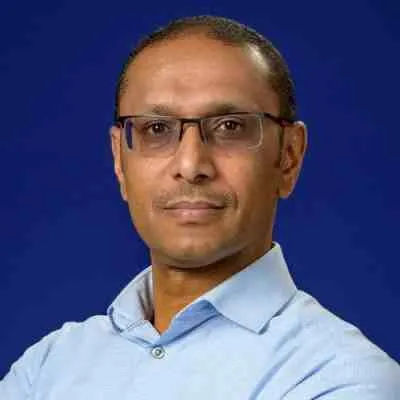 Professional headshot of a man with glasses, wearing a light blue shirt, set against a solid blue background. The image conveys a confident and approachable demeanor, suitable for a corporate or professional context.