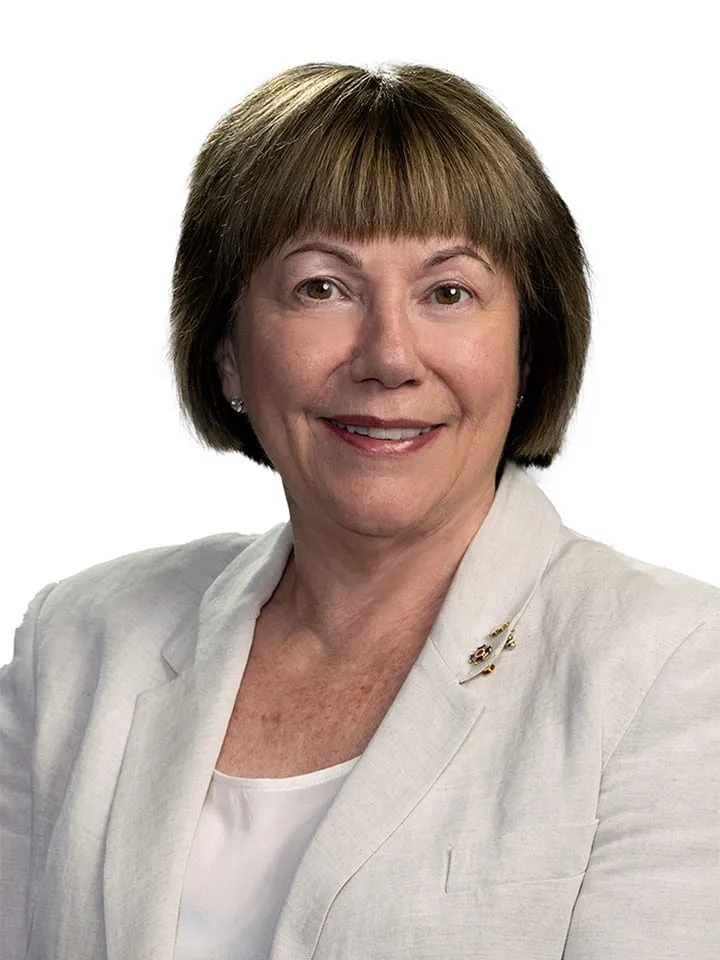 Portrait of a middle-aged woman with short brown hair, wearing a light-colored blazer and a white top, smiling against a plain white background.