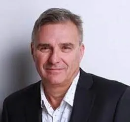 Professional headshot of a middle-aged man in a black blazer and white shirt with a subtle pattern, smiling against a neutral background, suitable for business profiles or corporate websites.
