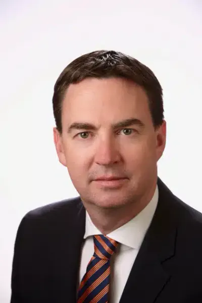 Professional headshot of a businessman wearing a dark suit and striped tie, with a neutral background, conveying a confident and approachable demeanor.